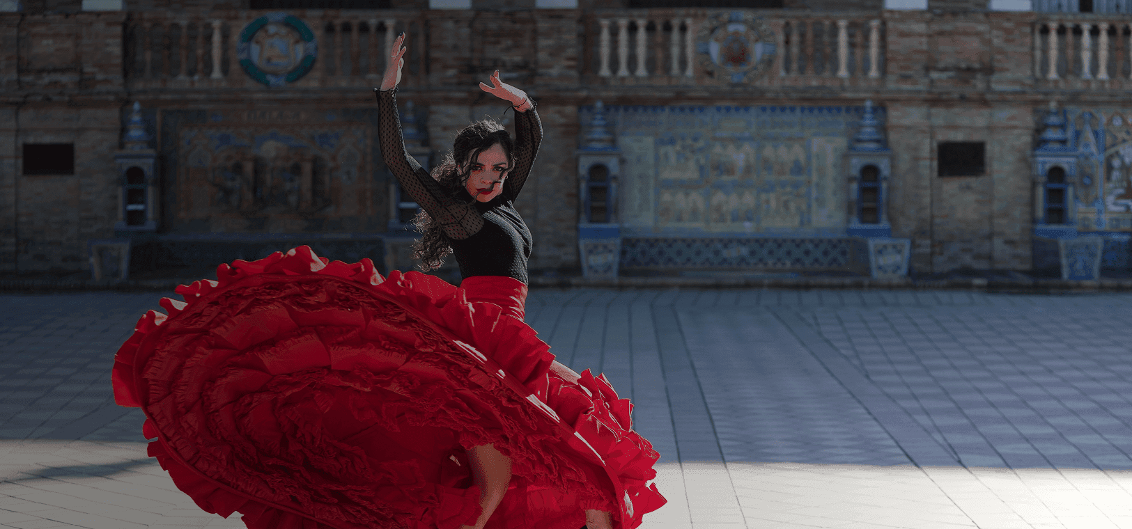 Flamenco dancer twirls in front of grand building backdrop. Overlaid is the Spanish word "bailar" with its English translation, "to dance".
