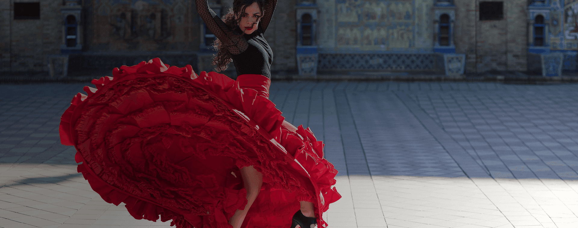 Flamenco dancer twirls in front of grand building backdrop. Overlaid is the Spanish word "bailar" with its English translation, "to dance".