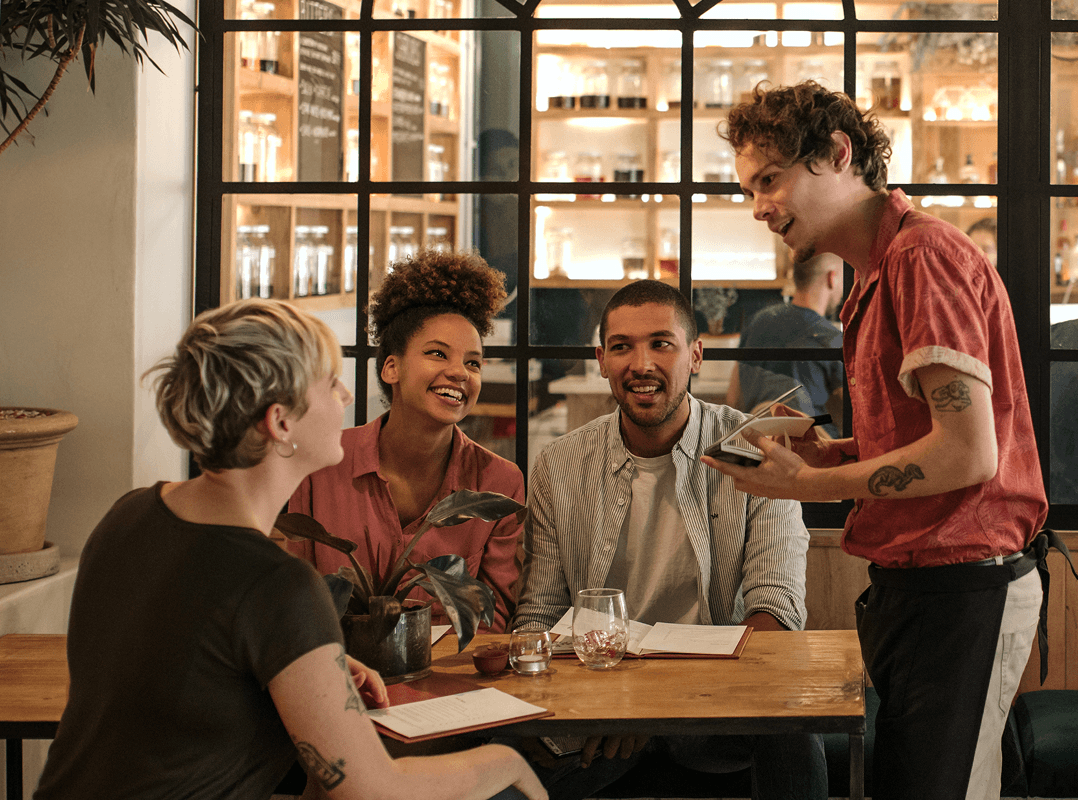 Group of friends practice a new language they have learned as they order from a waiter in a stylish cafe.