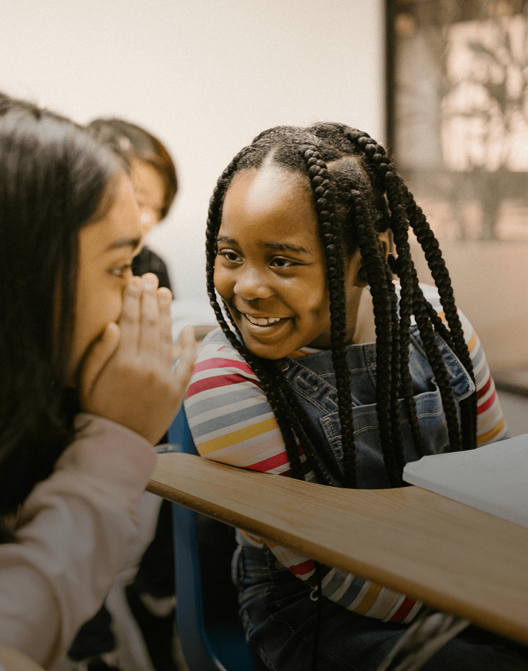 Smiling students whisper to each other as they learn a new language in school.